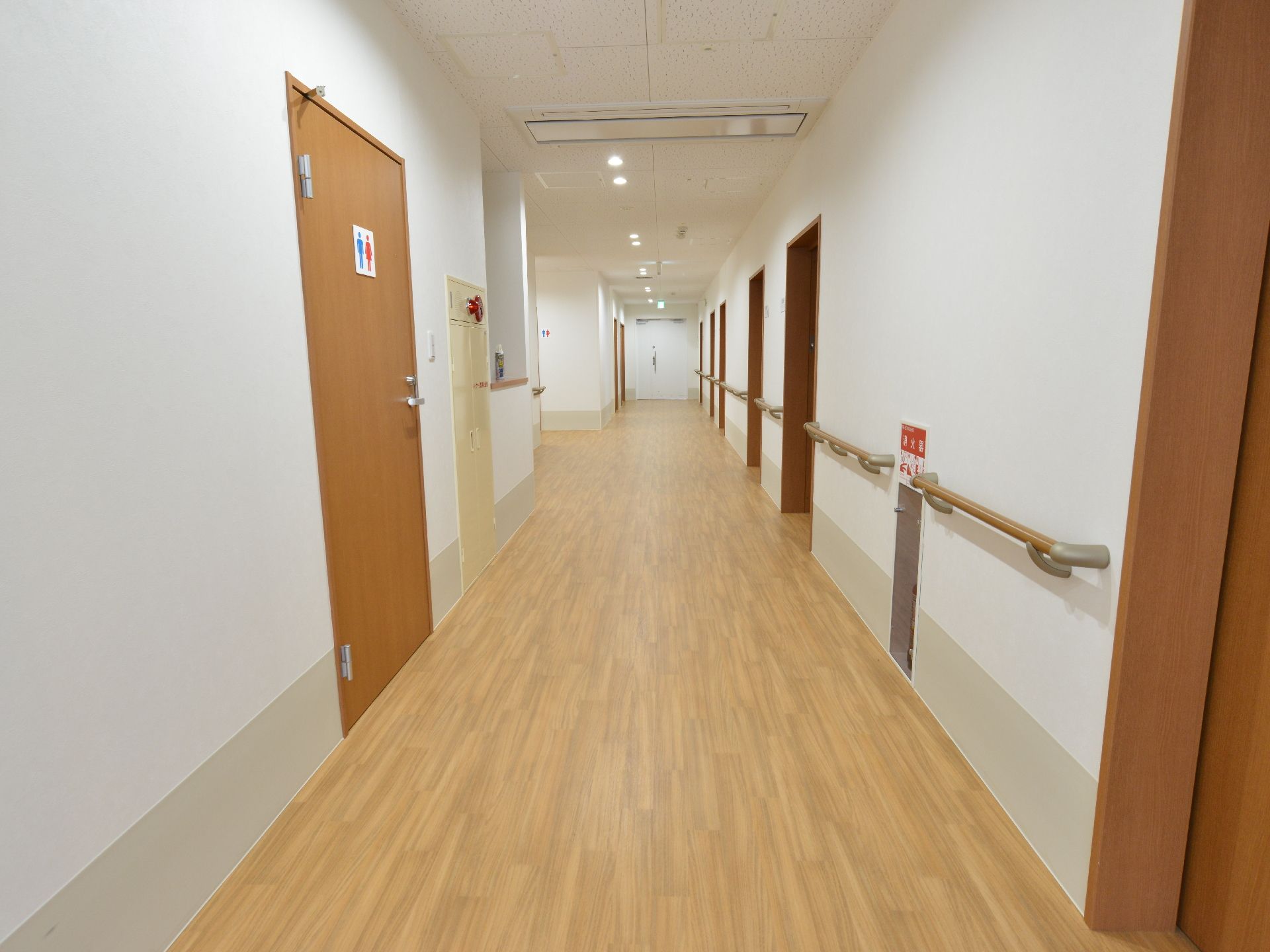 左手に共有のトイレのドアと消火栓がある。右手には居室のドアが並んでいる。また右手の壁には手すりが付けられ、消火器がある。