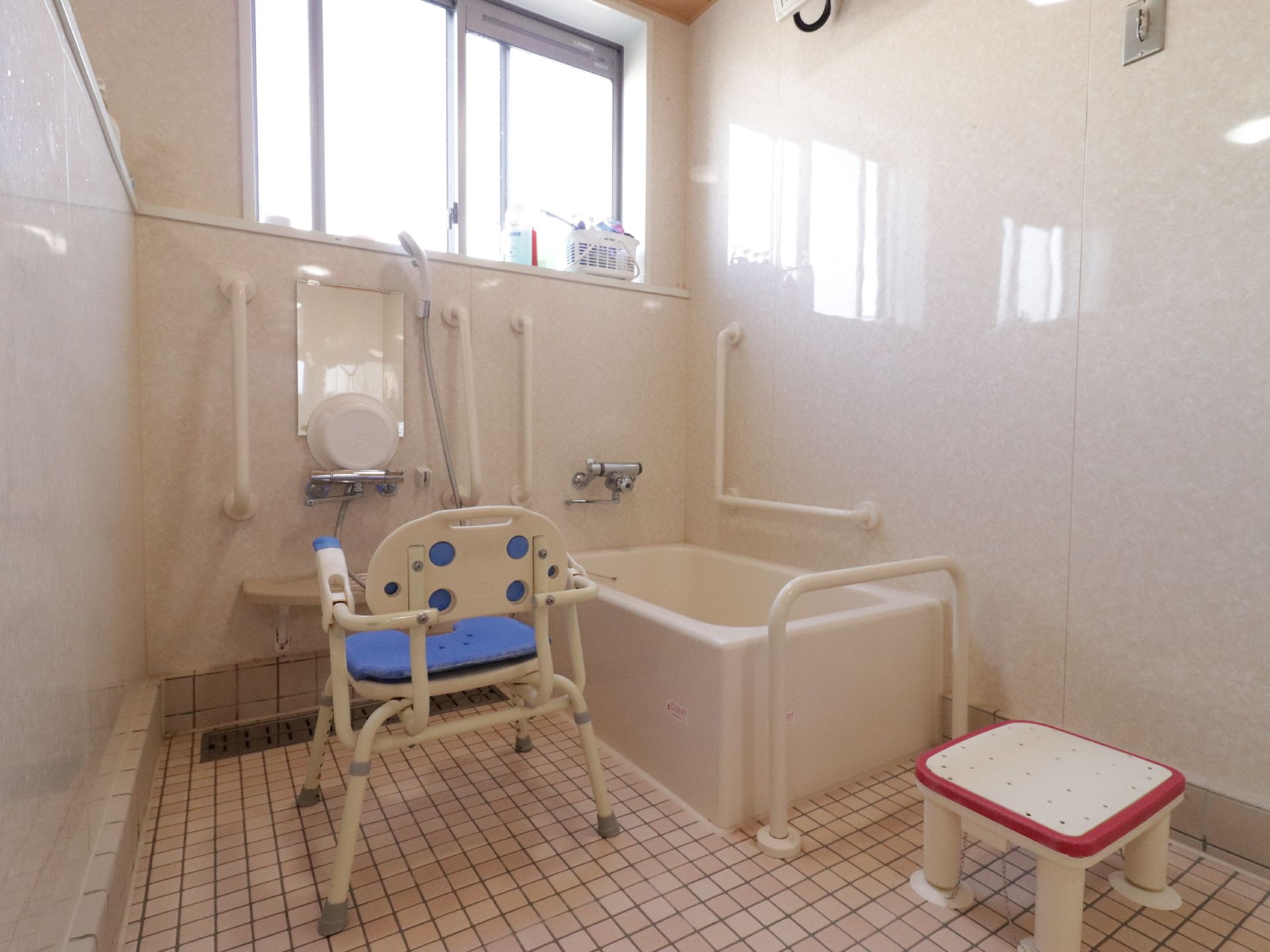 換気用の窓が付いたユニットバス、シャワーのあるお風呂場で、ふろ用専用椅子がおいてあるので、洗髪などが楽にできる。