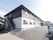 ２階部分は黒っぽく、１階部分は白い壁の建物である。奥に行くと、玄関がある。手前の外階段の近くに植物が植えてある。