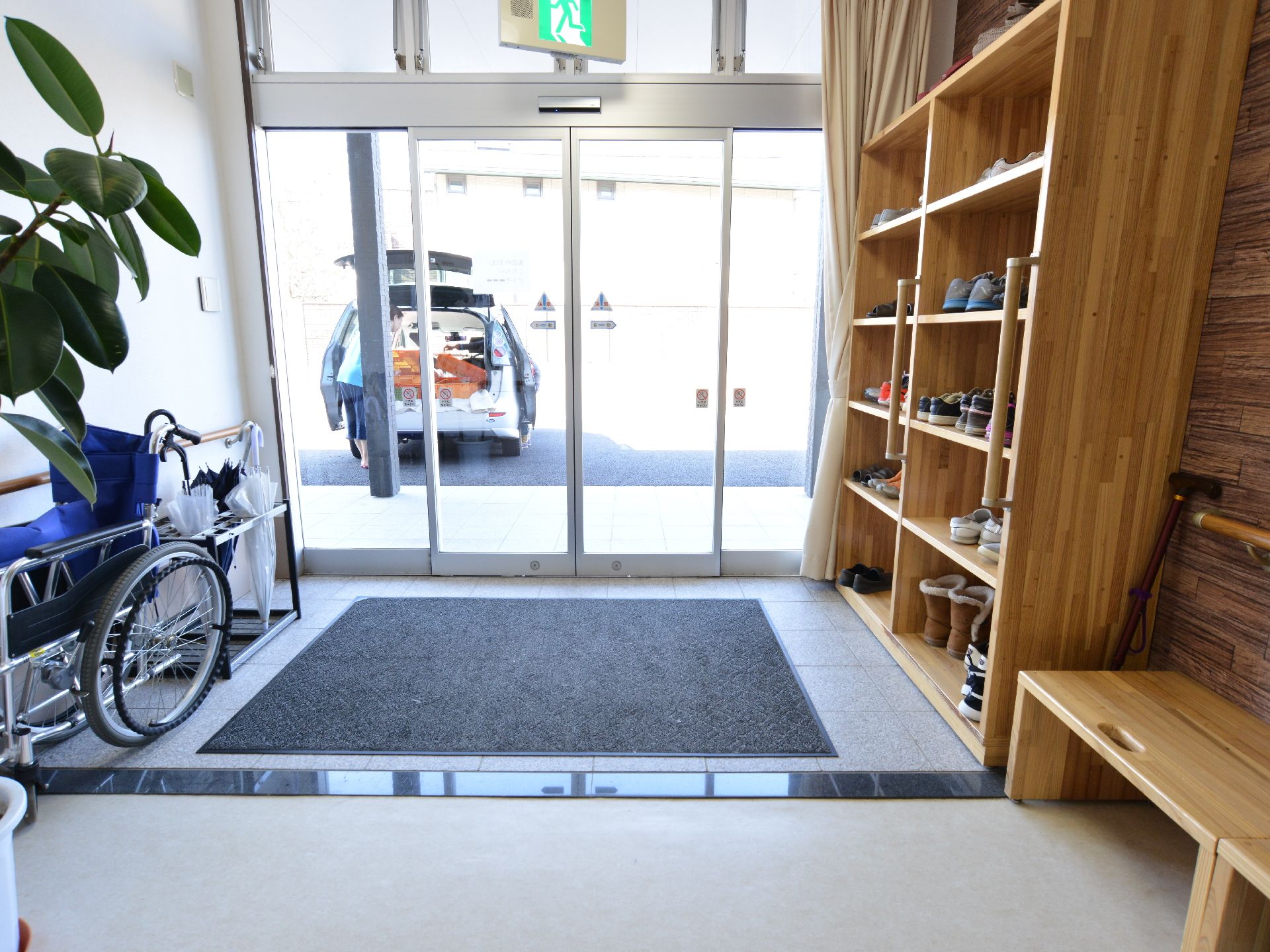 余裕を持った広さの玄関である。壁際には木製の下駄箱とベンチが設置されている。貸し出し用の車いすや傘立ても置かれている。