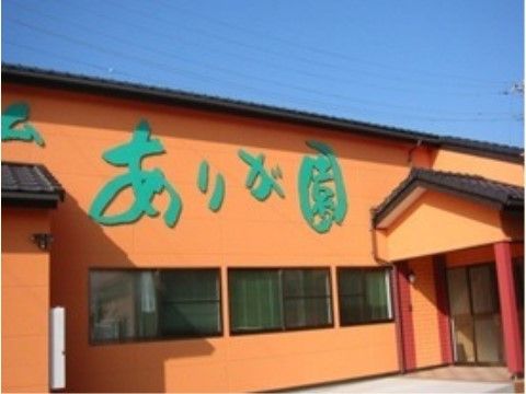 オレンジ色の外壁に、緑色の文字で園の名前が書いてある。屋根は褐色の瓦葺きで、玄関前にはひさしがある。
