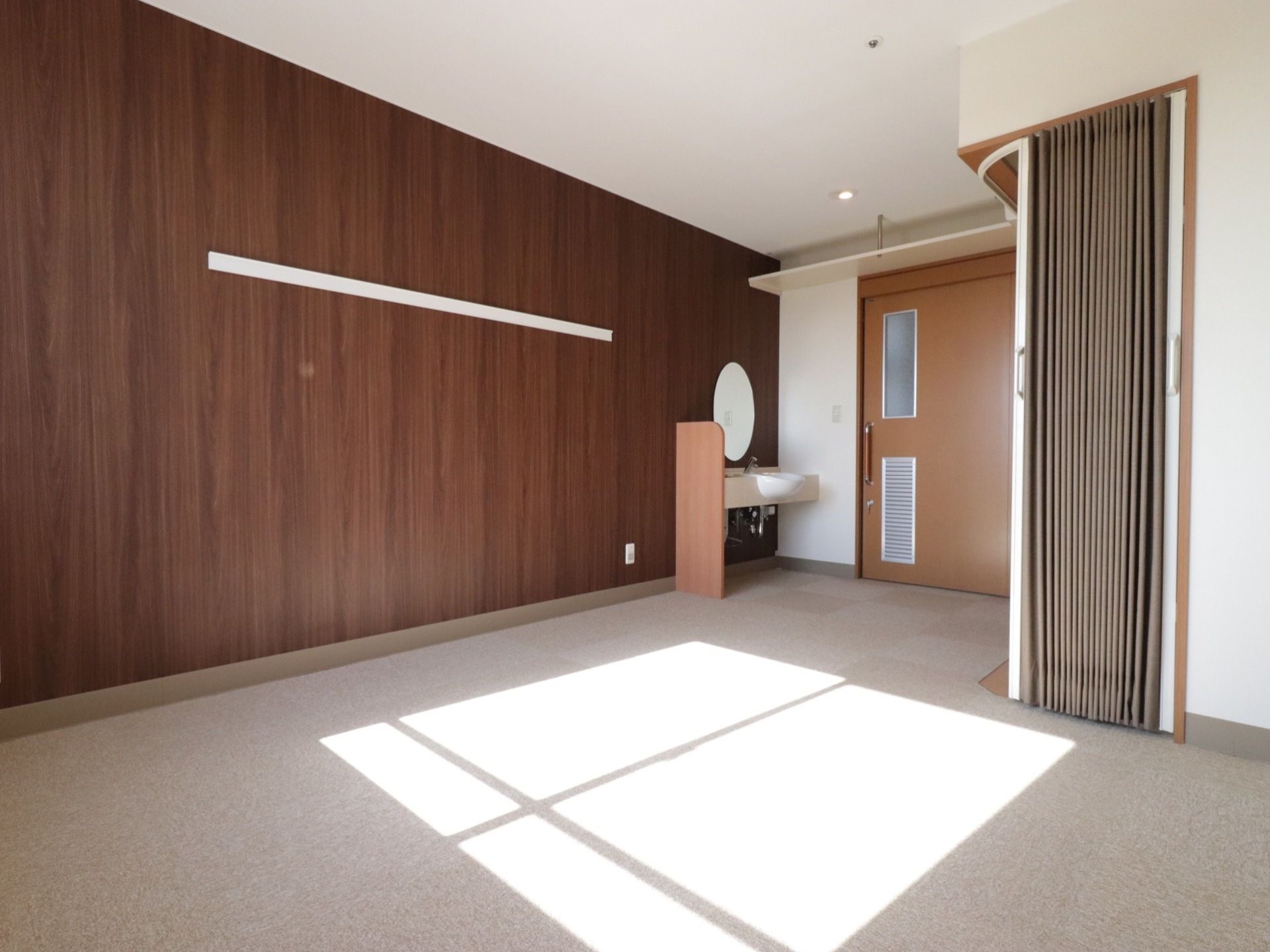 広く作られた居室。床は絨毯敷きになっており、スライド式ドアの入口の脇には丸い鏡のある洗面台が設置されている。