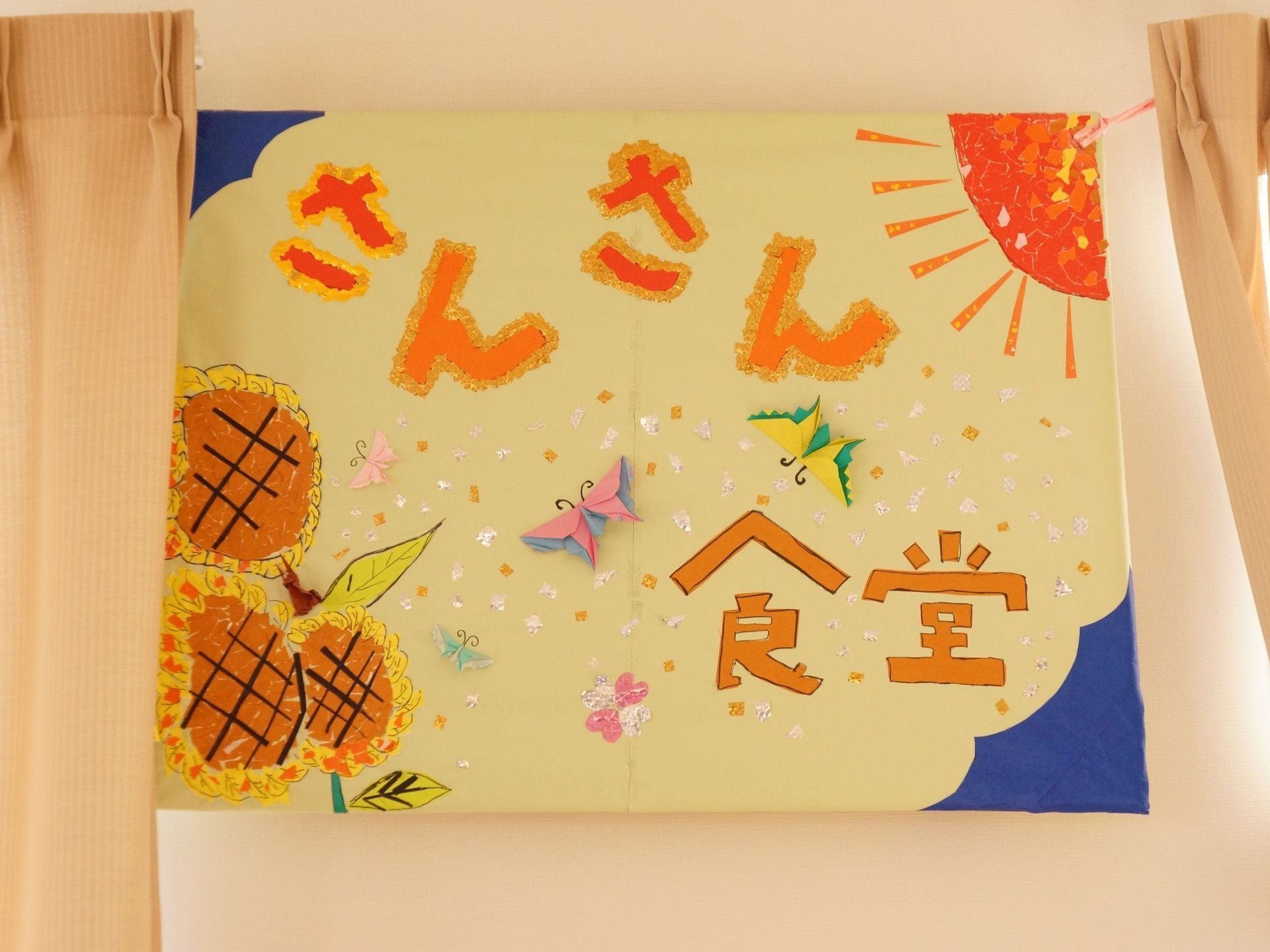 食堂名の看板が壁に設置されている。明るい雰囲気の鮮やかな色遣いで、大きな文字のわかりやすい看板になっている。