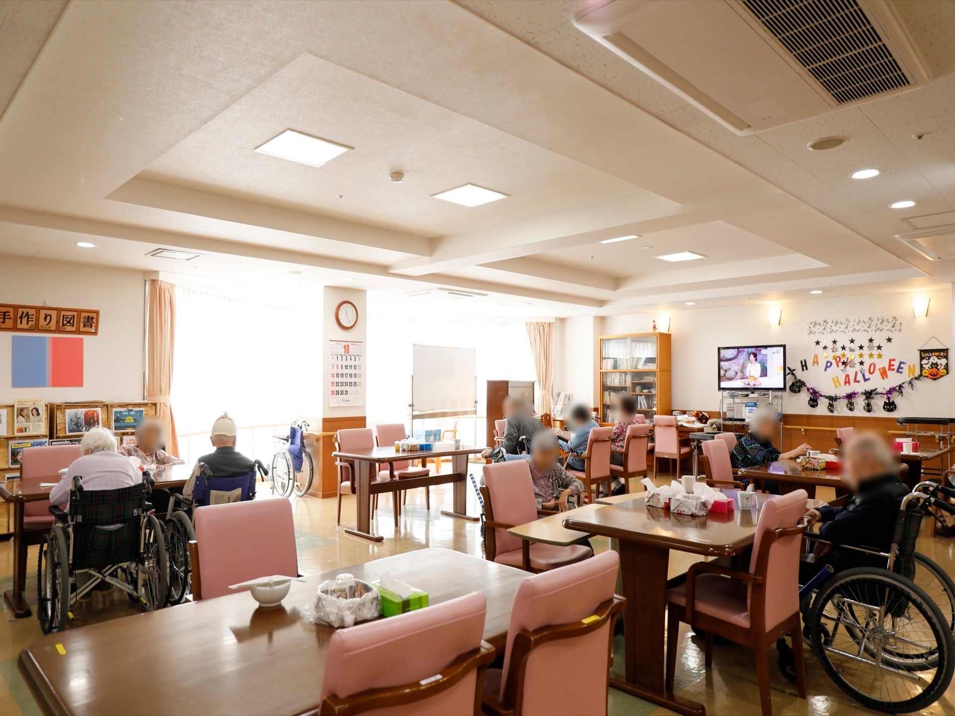 食堂に多くの椅子やテーブルが置かれている。壁面近くにテレビが設置されている。季節のイベントの飾りつけがされている。