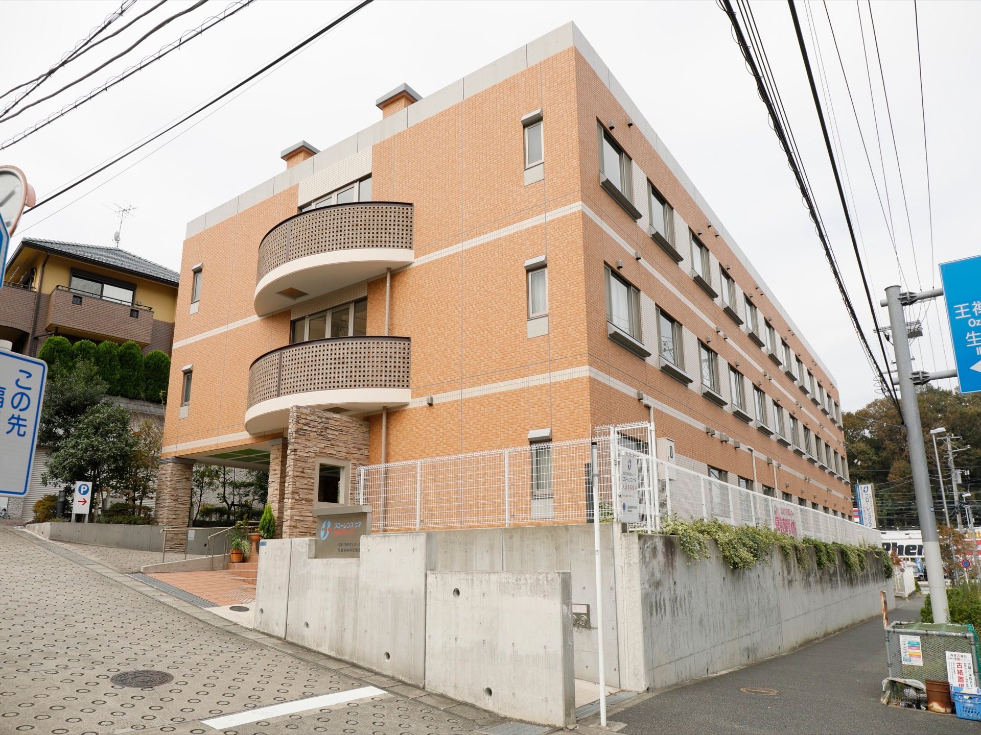 茶色系統の外壁のすっきりとした３階建ての施設である。大きな道路から少し坂を上がった所に、玄関への階段やスロープがある。