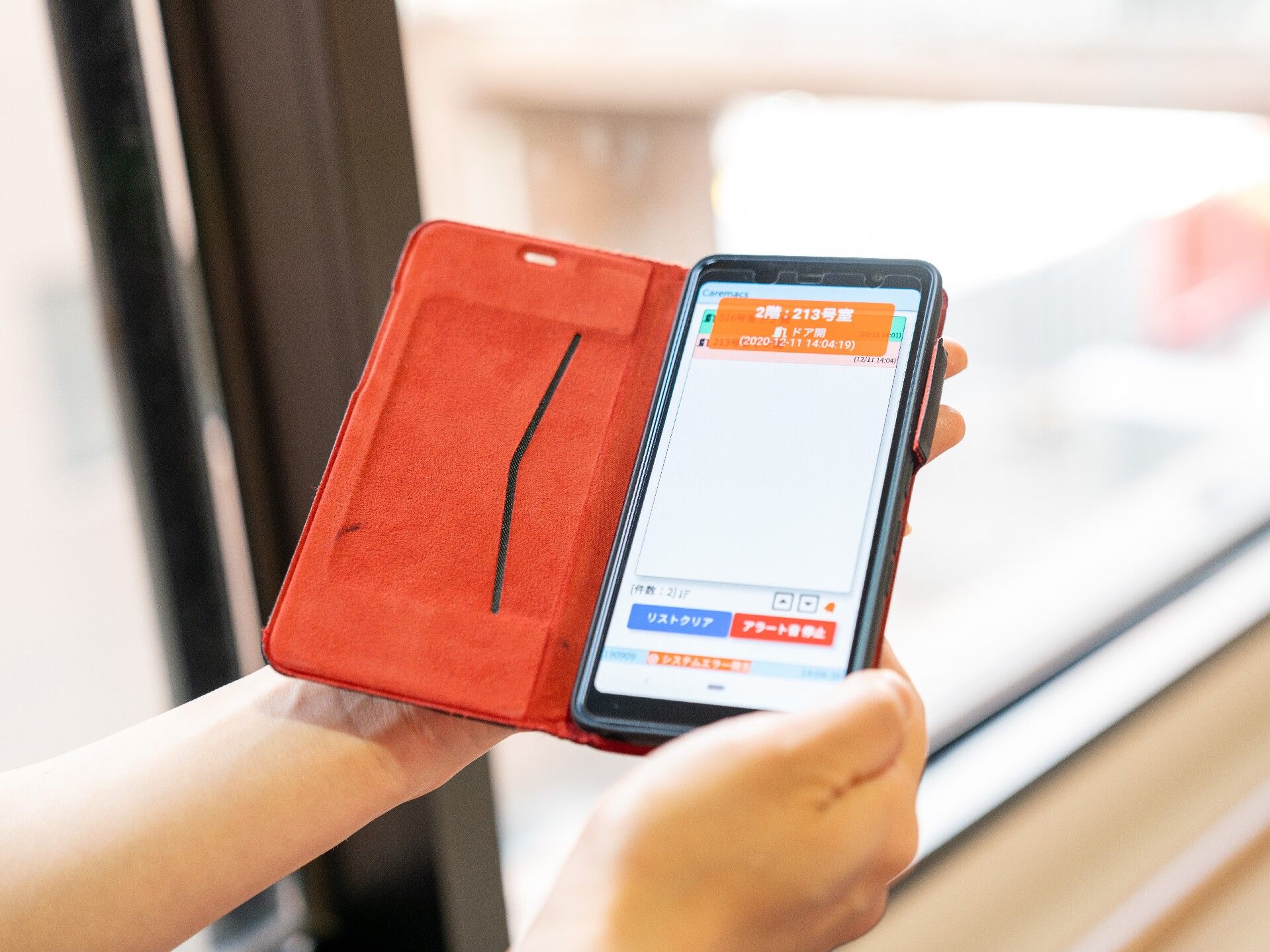 オレンジのスマホカバーの中にあるスマホの画面には何かのシステムが表示されている。