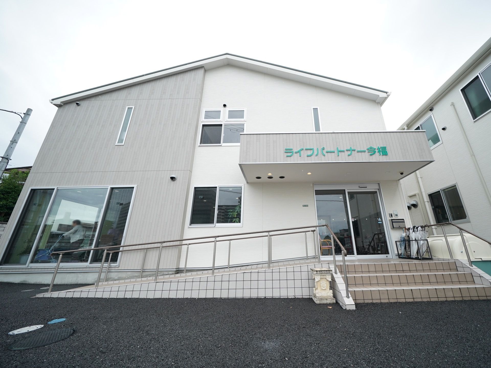 白と薄いグレーに塗り分けられた建物である。三角屋根の２階建ての建物で、玄関には階段とスロープが用意されている。