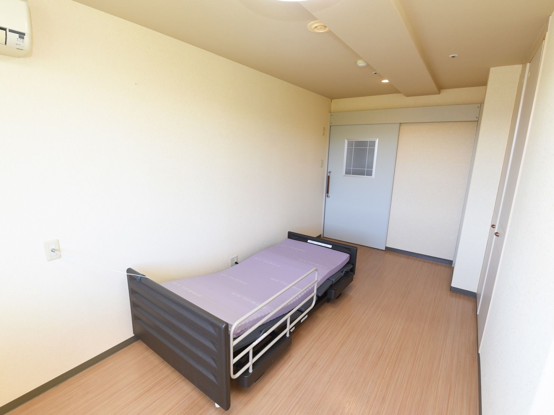 冷暖房設備や介護ベッド、クローゼットが完備された居室である。広めの間取りになっており、ナースコールが壁に設置されている。