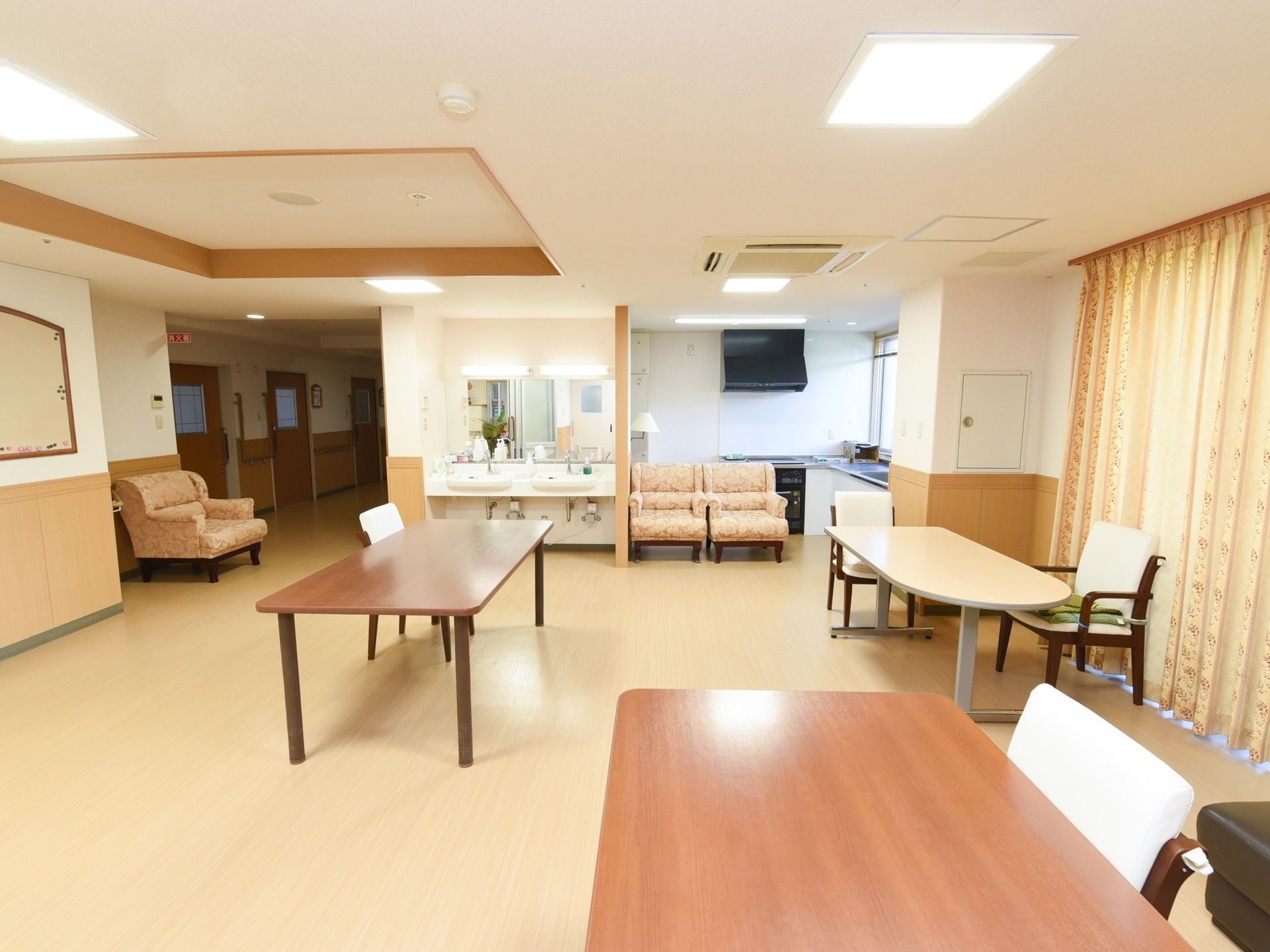 キッチンと洗面台が併設された共有スペースである。複数の椅子とテーブルが設置されている。照明も多く明るい。