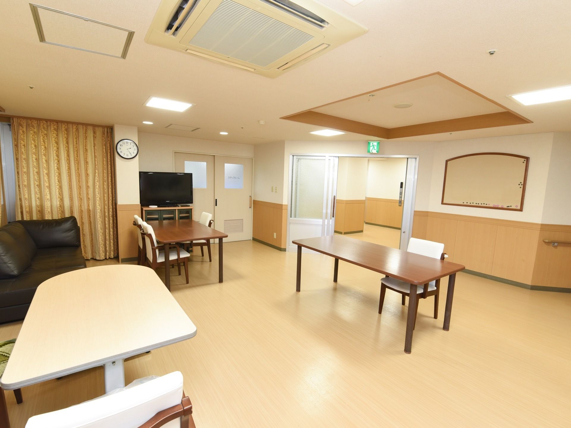 テレビが設置してある共有スペースである。壁には掲示物を貼るボードや手すりがあり、冷暖房設備も完備している。
