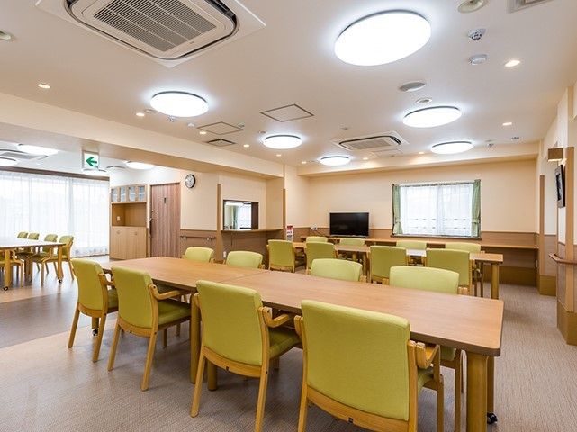 広い室内に、長テーブルを囲み椅子が８脚ずつ置かれたダイニングセットが３つ並んでいる。壁には手すりがあり、角には樹脂製のカバーが付いている。