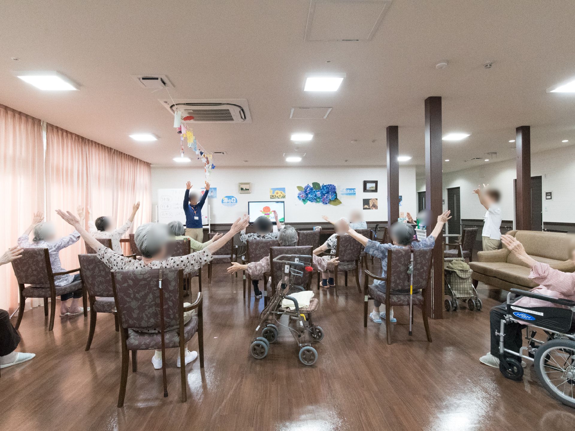 広いスペースに椅子を並べ、入居者が簡単な体操を行っている。椅子と椅子の間隔を広く取り、大きく手を広げても大丈夫なようにしている。