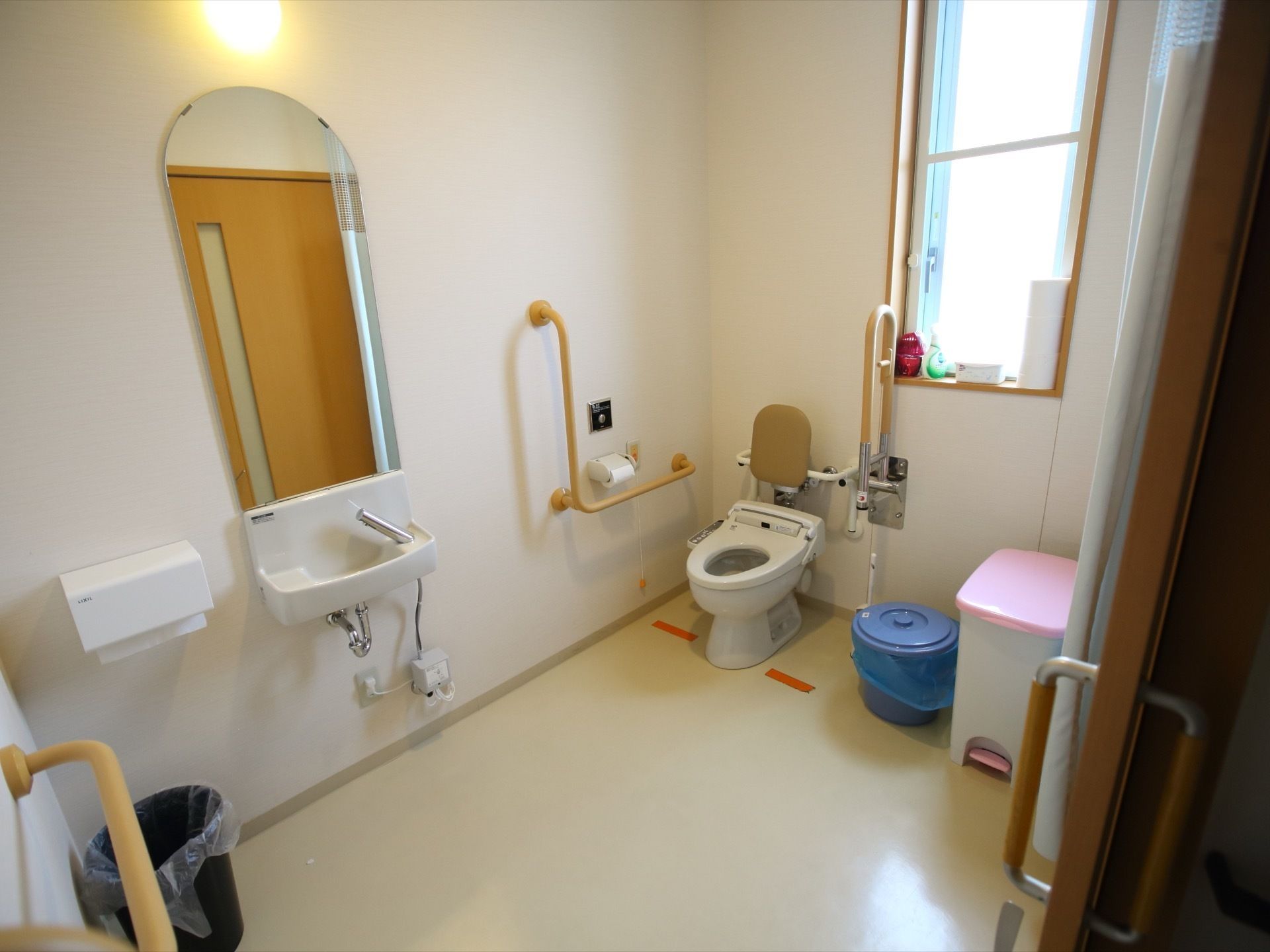 トイレはとても広いスペースがあり、奥には背もたれの付いた温水洗浄便座がある。壁には手すりがかかっている。