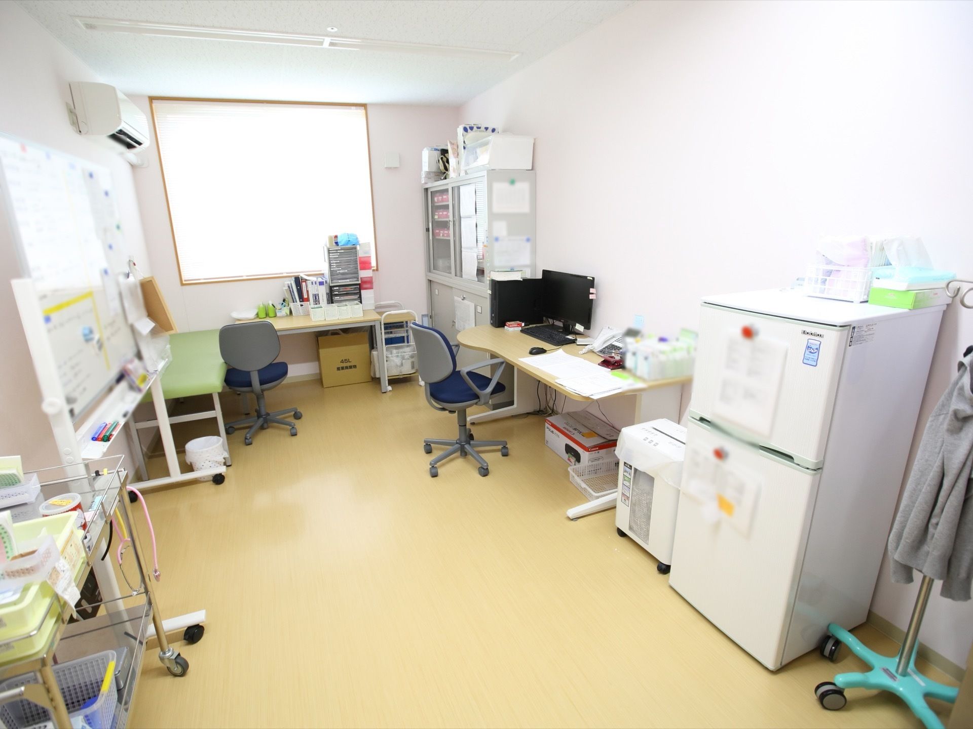 医務室には冷蔵庫やデスク、椅子が置いてある。奥には大きい窓があり、壁の上にはエアコンがある。