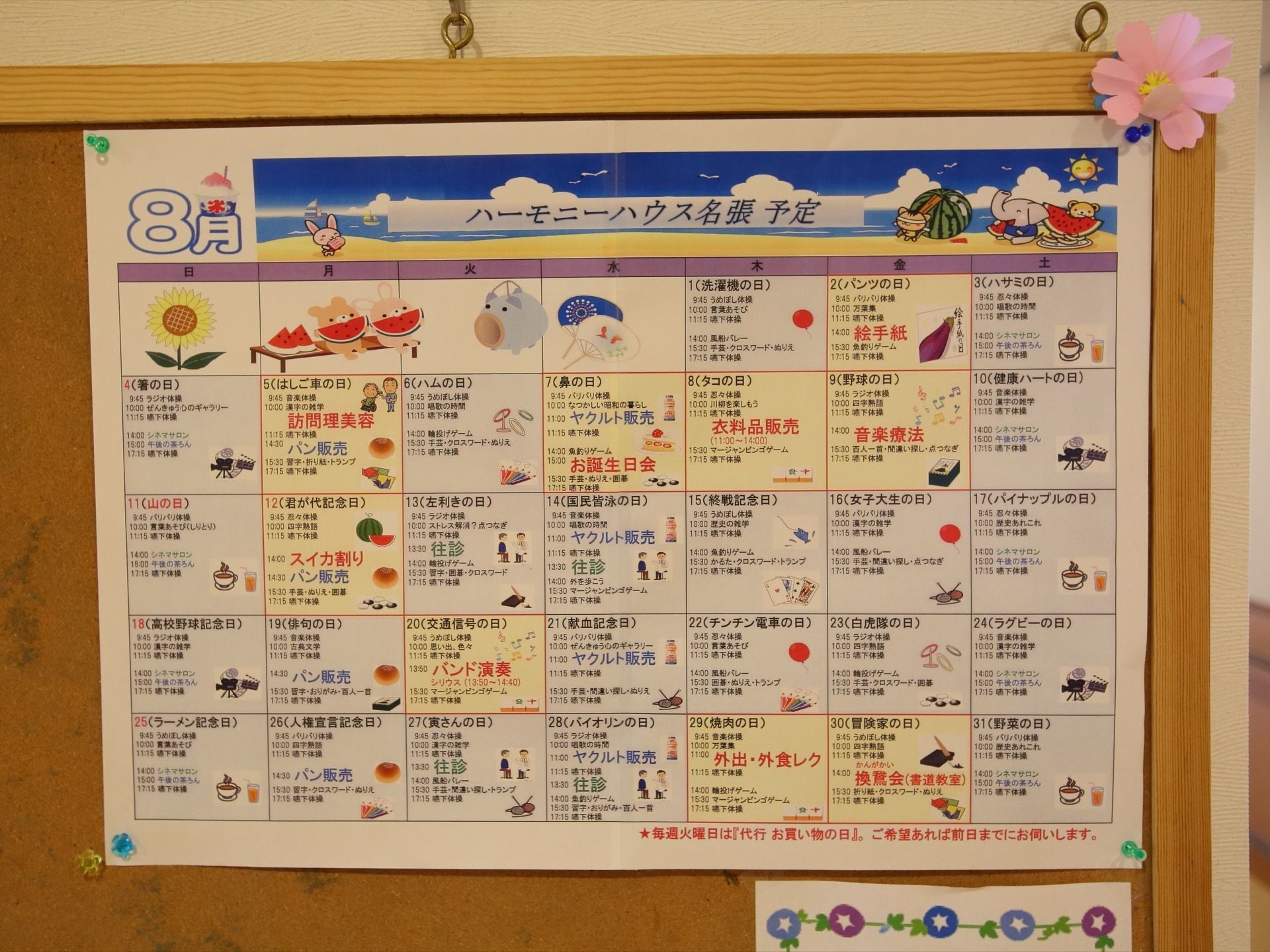 壁に取り付けられたコルクボードに掲示物が貼られている。予定表が画びょうで止められており、端には花の飾りが付けられている。