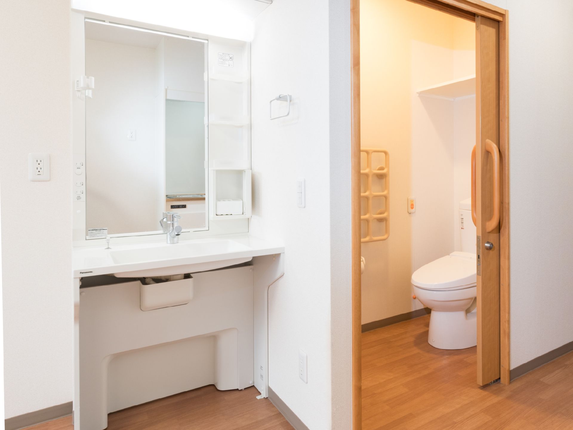 備え付けのトイレと洗面台である。トイレ引き戸で、個室内にナースコールが備わっている。洗面台には収納棚や鏡が付いている。