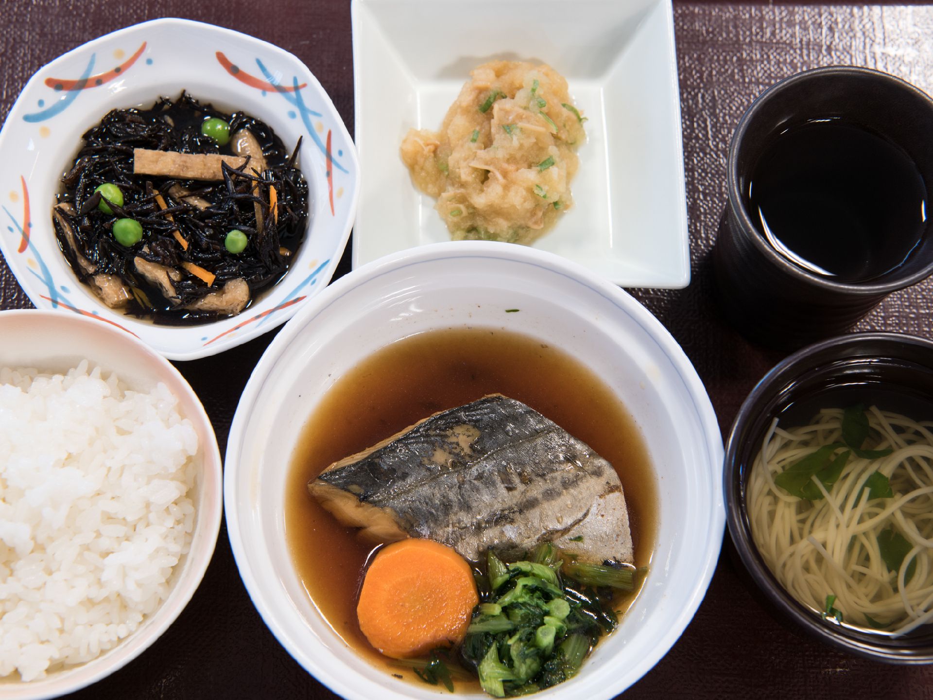 ご飯と汁物、メインの魚のおかずと、副菜が2種類、お茶が黒いトレーの上に乗っている。柔らかく食べやすそうなメニューである。