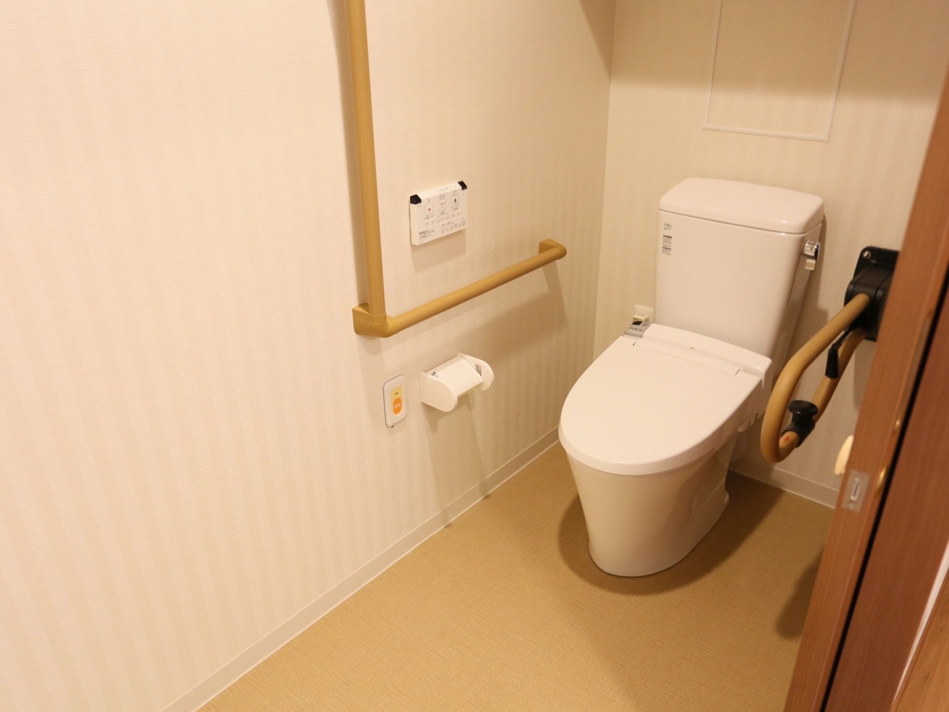 トイレには洋式便器があり、便器の前方は広くなっている。壁側には手すりが取り付けられており、手すりの下には呼び出しボタンが設置されている。