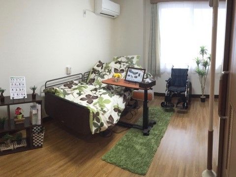 大きな窓からの採光で明るいお部屋である。サイドテーブルや車椅子なども配備されており安心である。観葉植物などを設置して心穏やかに過ごせる。