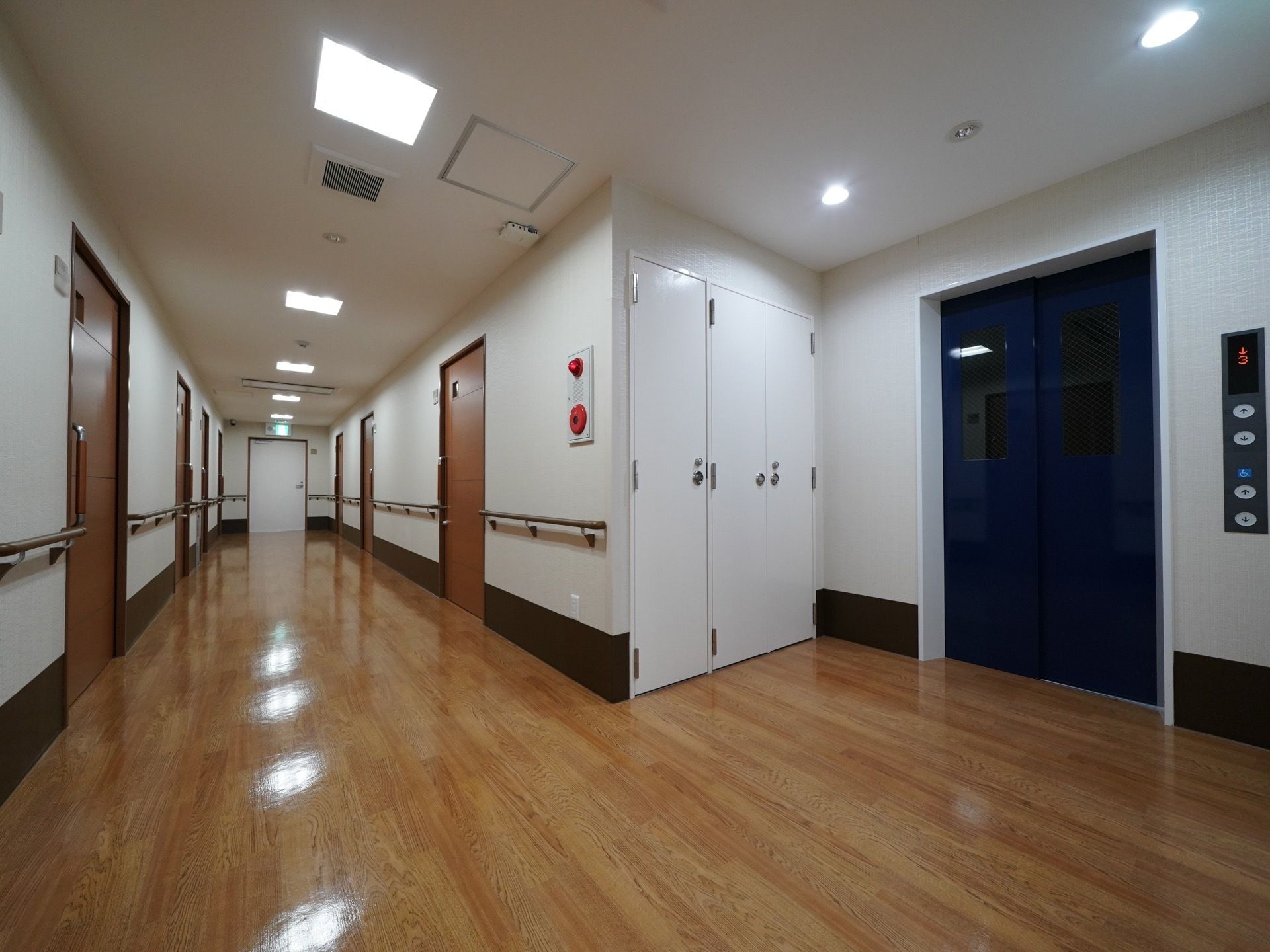 綺麗に磨かれたフローリングの中廊下が伸びている。エレベーターと、居室の扉が並んでいる。照明が等間隔で点灯していて明るい。