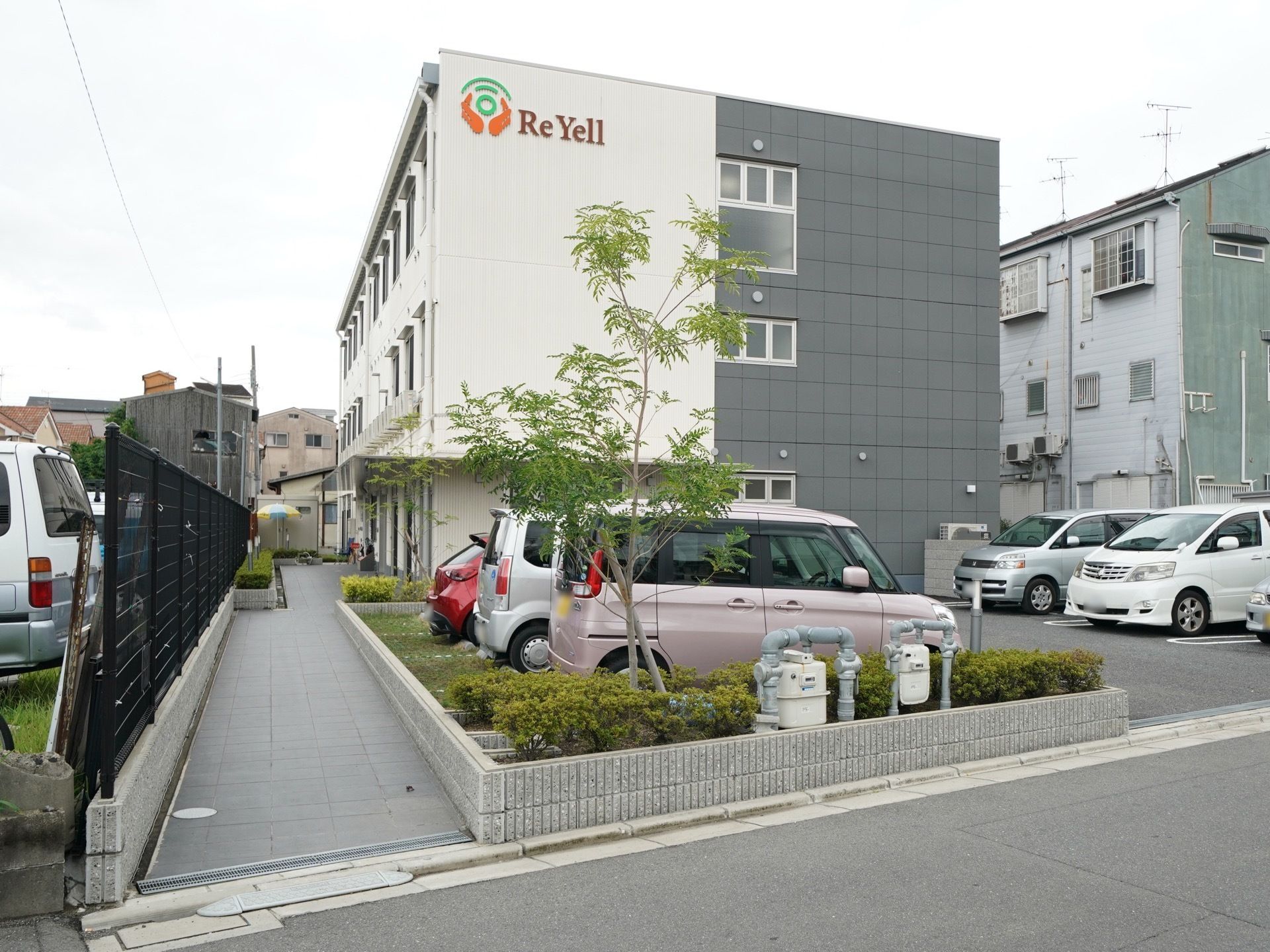 住宅街の中にホームの建物が建っている。車椅子をご利用の方のために、道路と敷地の間の段差には補助ブロックが置かれている。