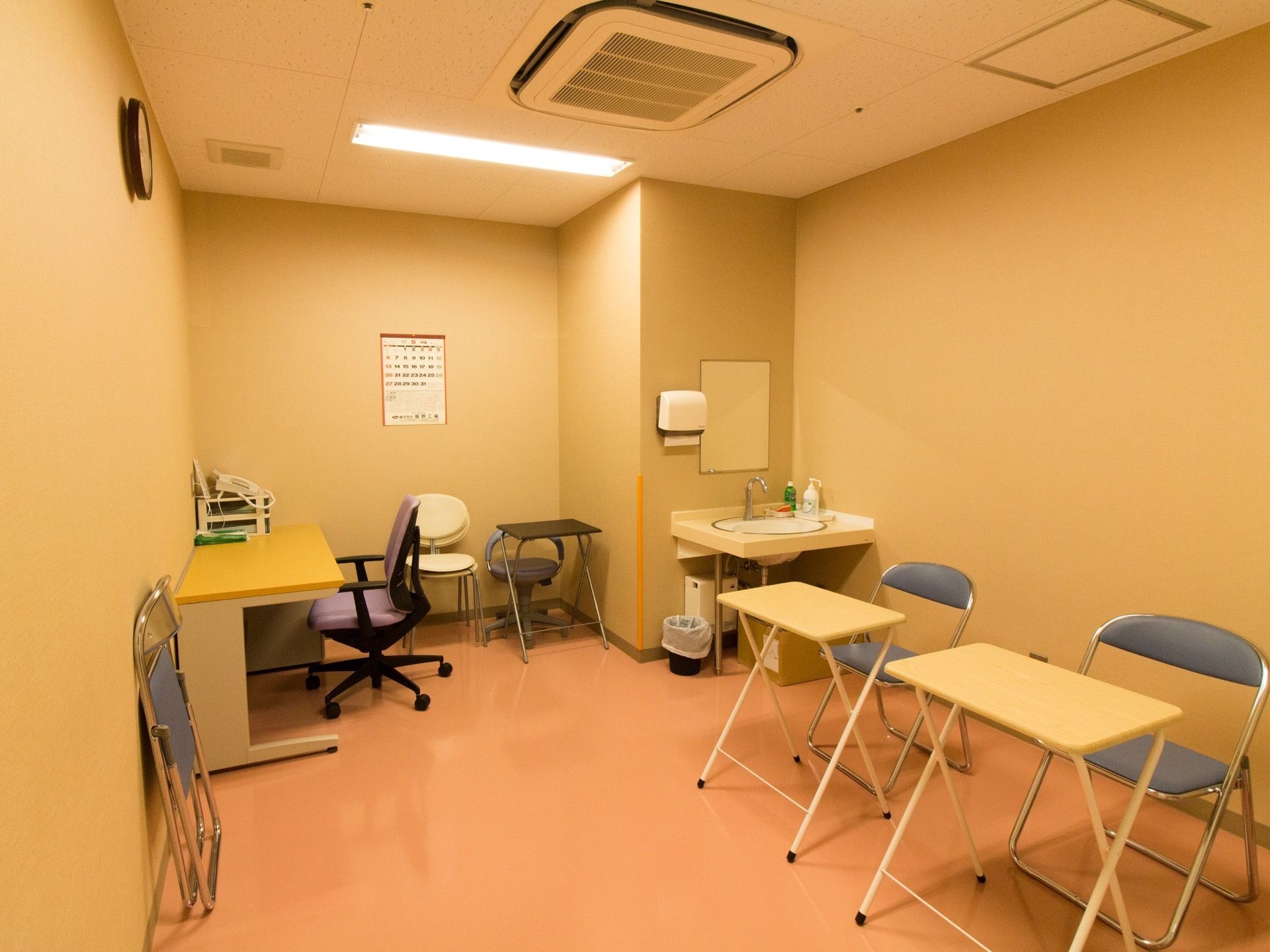 部屋の中に机と椅子のセットが２つある。壁にそって設置されている机の横に電話がある。洗面台も完備されている。