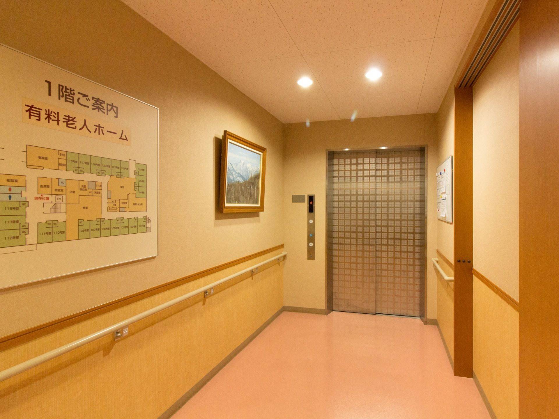 広い通路の突き当りにエレベーターがある。近くの壁には施設内の見取り図を掲示し、手すりを取り付けている。