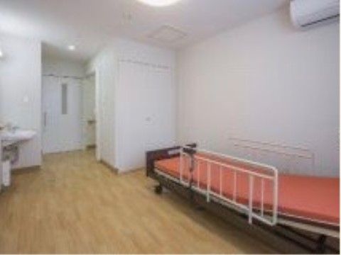 寝台が動く介護用ベッドがあり、片側が少し上がっている。床は一面フローリングで、明るい照明に照らされている。
