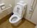 白い壁とフローリングの床のスペースに洋式トイレが設置されている。便器の両側に手すりが設置されていて、左側は可動式になっている。