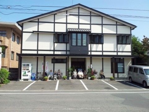 外で日向ぼっこしながら語り合っているご入居者様と施設の外観