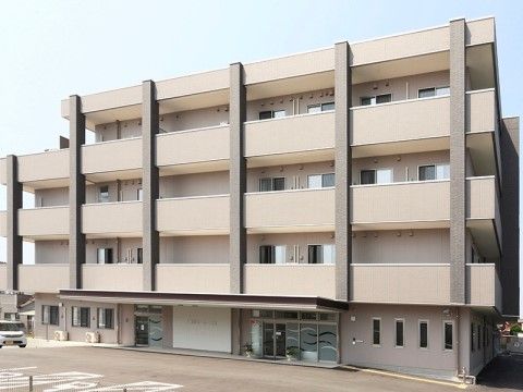 駐車スペースも広く持つ、オフホワイトを基調とした5階建ての施設の外観