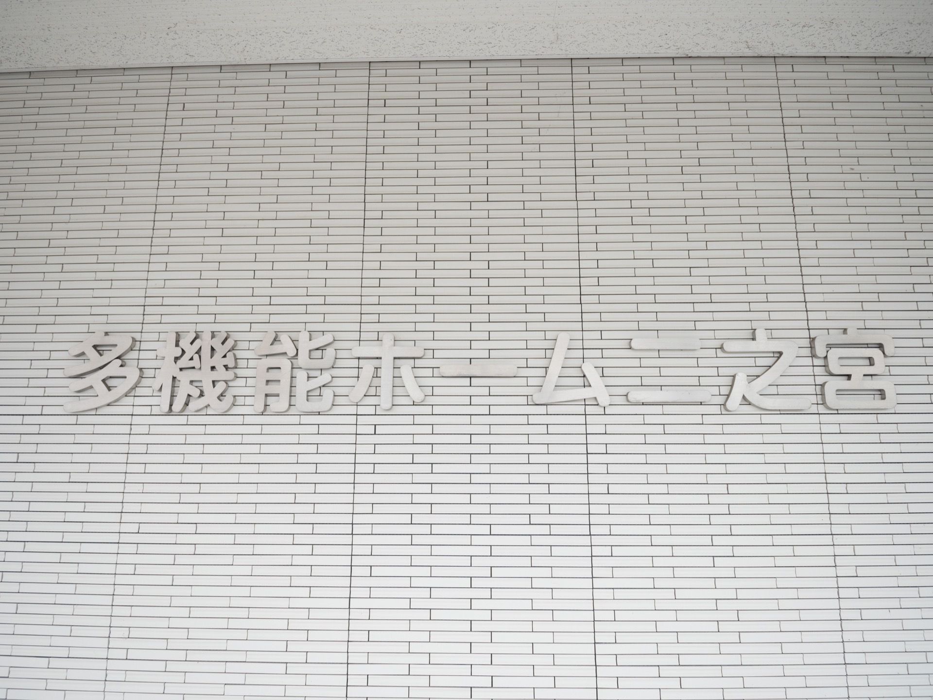 白を基調とした清潔感のある外壁に、シルバーの文字で施設名が書かれている。上には屋根が設置されている。