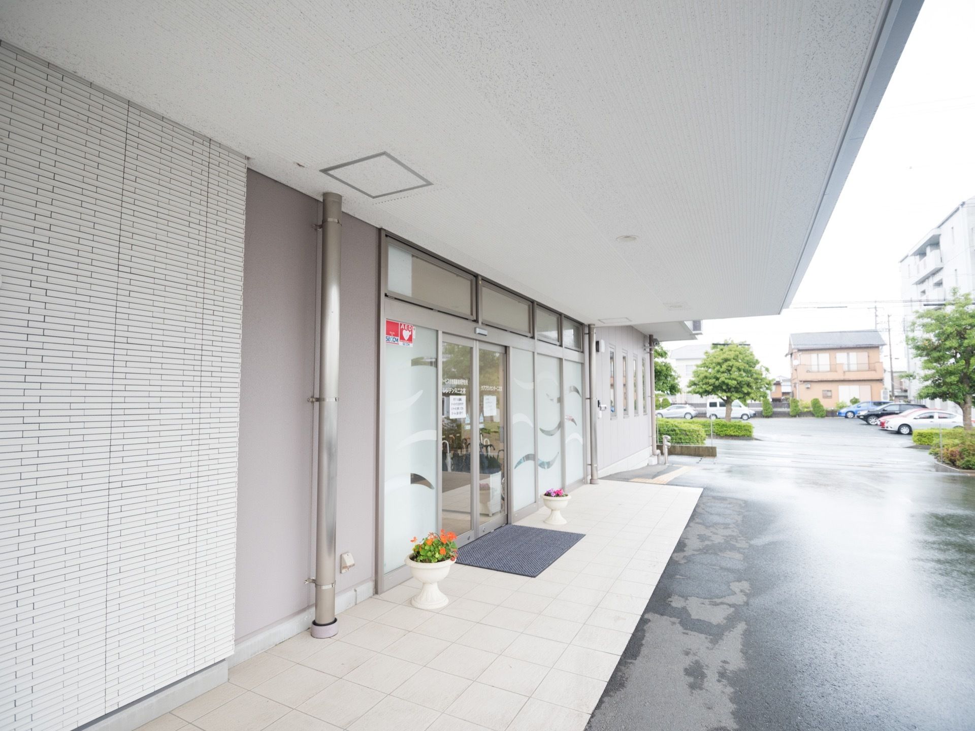 玄関前はひさしがついており、直接雨が当たらないようになっている。自動ドアの両脇には、白い植木鉢が飾られている。