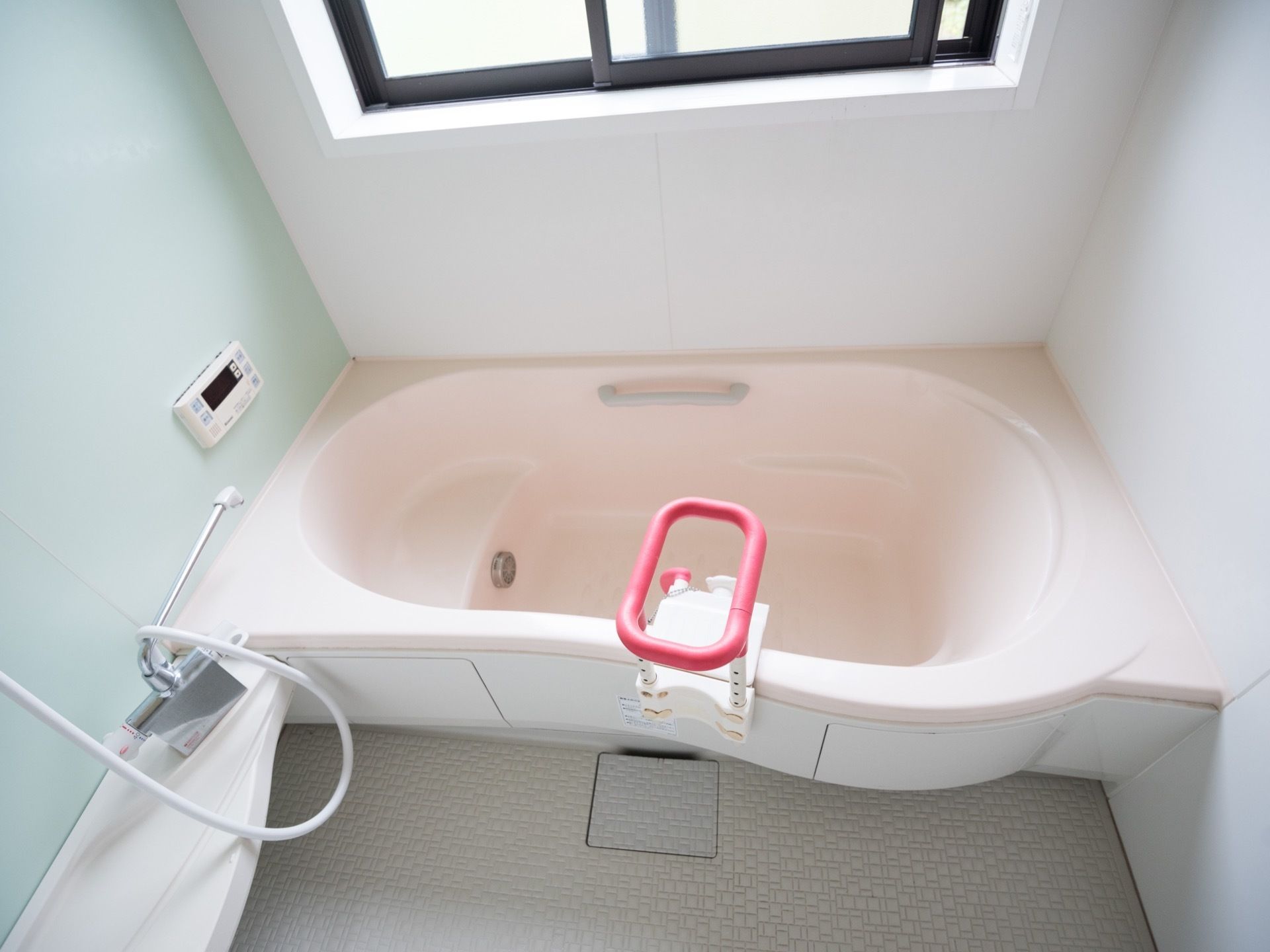 淡いブルーとピンクを使用した、温かみを感じる明るい浴室である。シャワーやにぎりやすい手すりが完備されている。