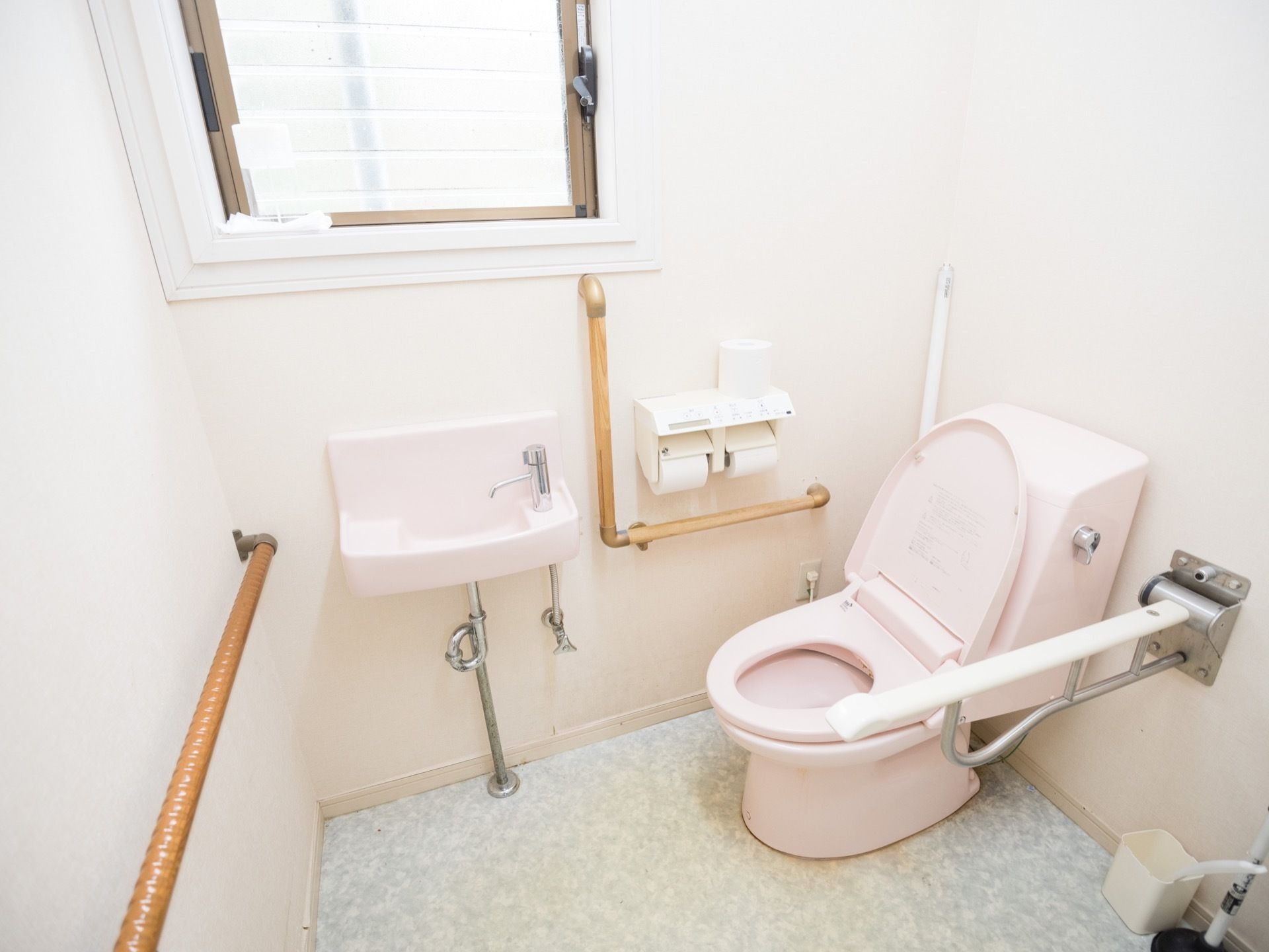 淡いピンクで統一された優しい雰囲気が感じられるトイレである。可動式の手すりや洗面スペースが完備されている。