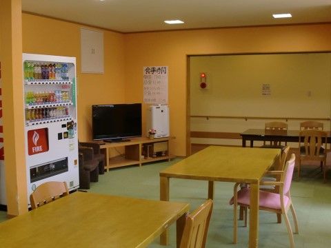 テーブルセットが２セットあり、椅子はすべて左の壁の方を向いている。右奥の出入り口は大きく開いており、手すりのついた廊下が見える。
