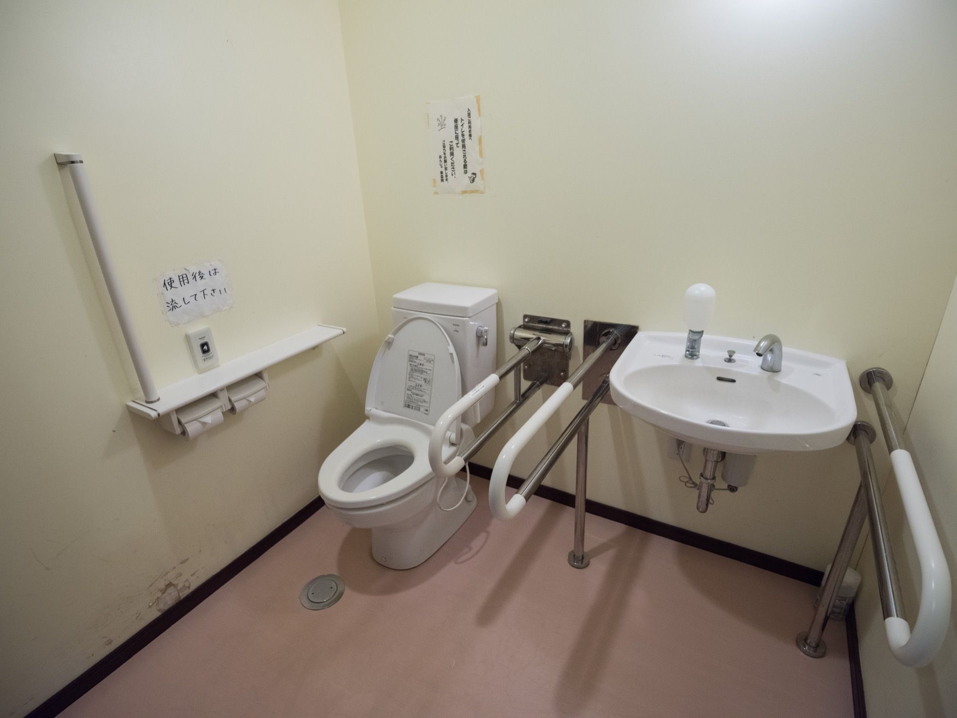 真っ白な壁と広々とした空間が特徴的な共有トイレである。温水洗浄便座や手すり、洗面スペースが完備されている。
