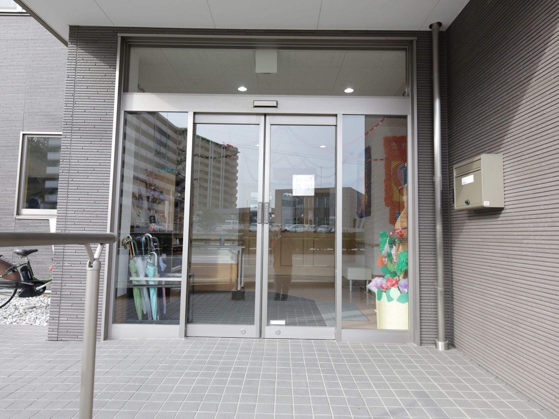 施設の建物はグレーの外装で、シックでおしゃれな外観。エントランスドアは両開きで、入居者様が出入りしやすく造られている。