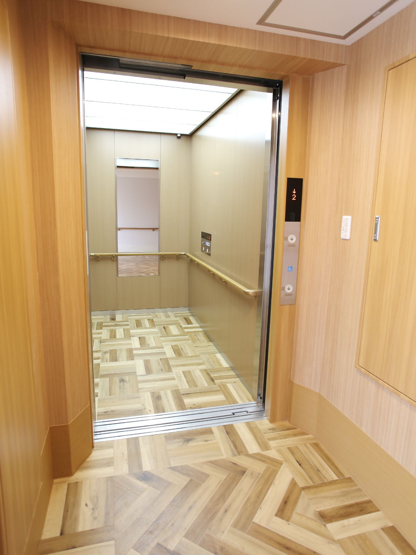 エレベーターの内部は縦長でとても広い。奥には鏡が設置されていて、壁には3面に手すりが付いている。上部は全面にライトがあり明るい。