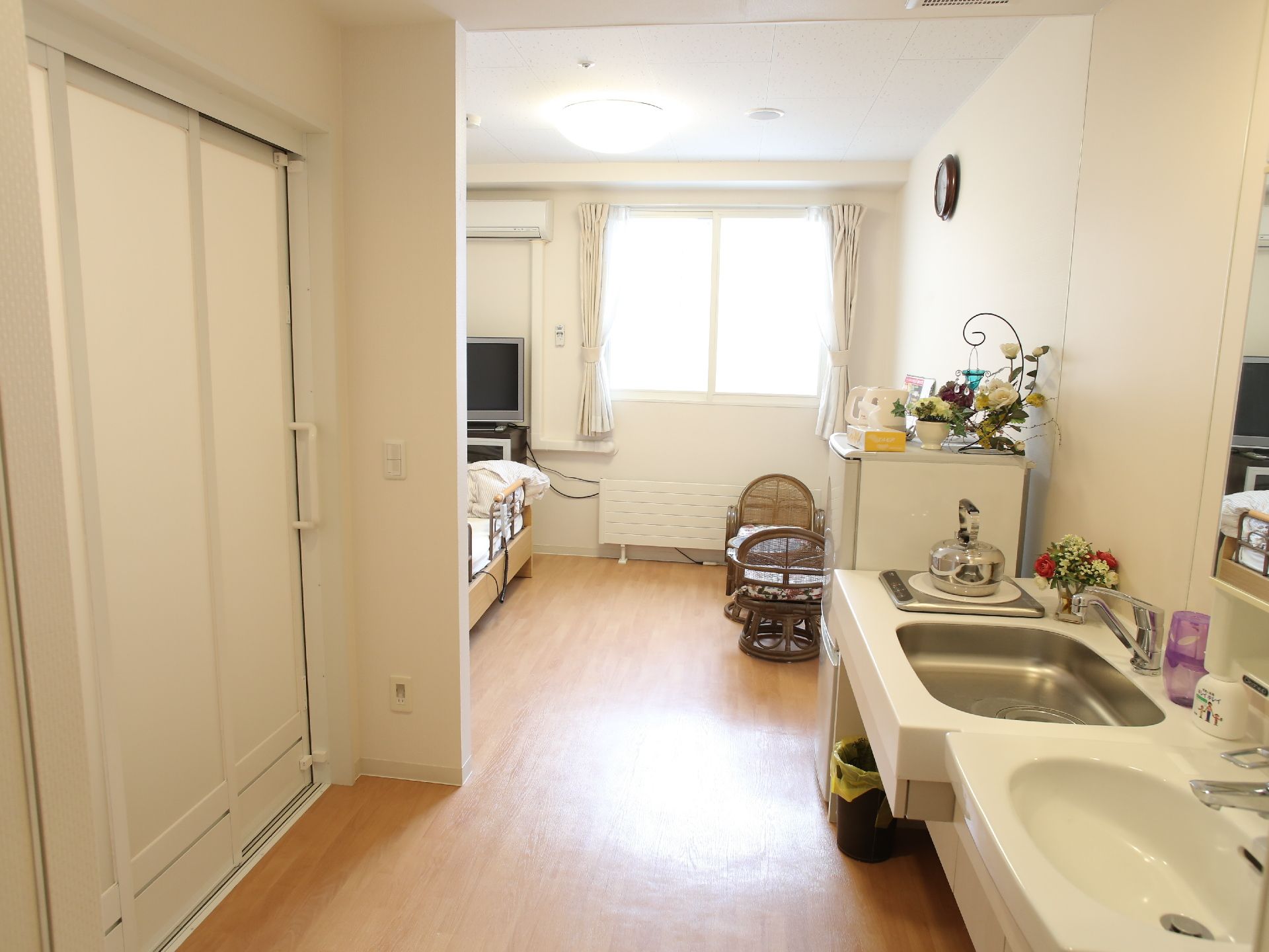 窓があり白で統一された明るい部屋。IHコンロや冷蔵庫が完備されており、なるべく自立できるようになっている。