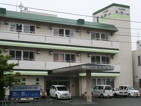外観は緑色の屋根の３階建てのビルのような建物である。アスファルトで舗装された敷地には数台の車が停められている。