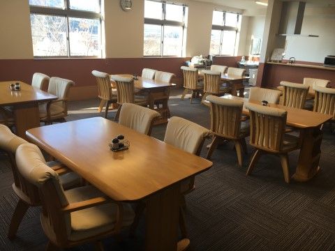 食堂は、茶色とグレーを基調とした落ち着いた色合いで統一されている。４脚の椅子に囲まれた長方形のテーブルが室内に複数台設置されている。