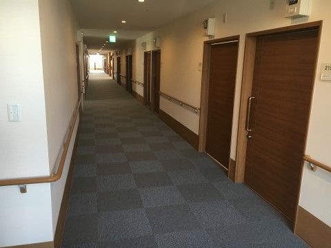入居者様の居室へと続くスライド式のドアは、非常に幅が広い仕様となっている。また、廊下の壁沿いには手すりが設置されている。