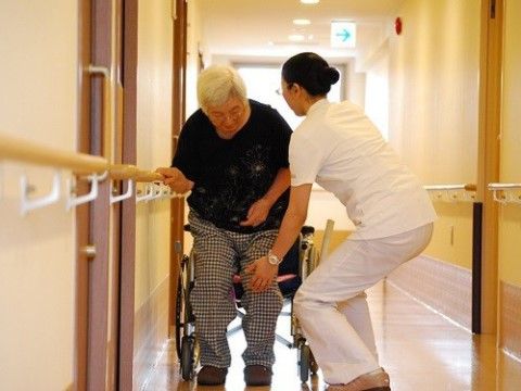ご入居者様が車いすにお座りになるところをサポートするスタッフ