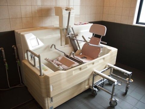 座ったまま浴槽内に移動できる機械浴が設置された浴室。窓も付き、壁にはタイルが貼られている。