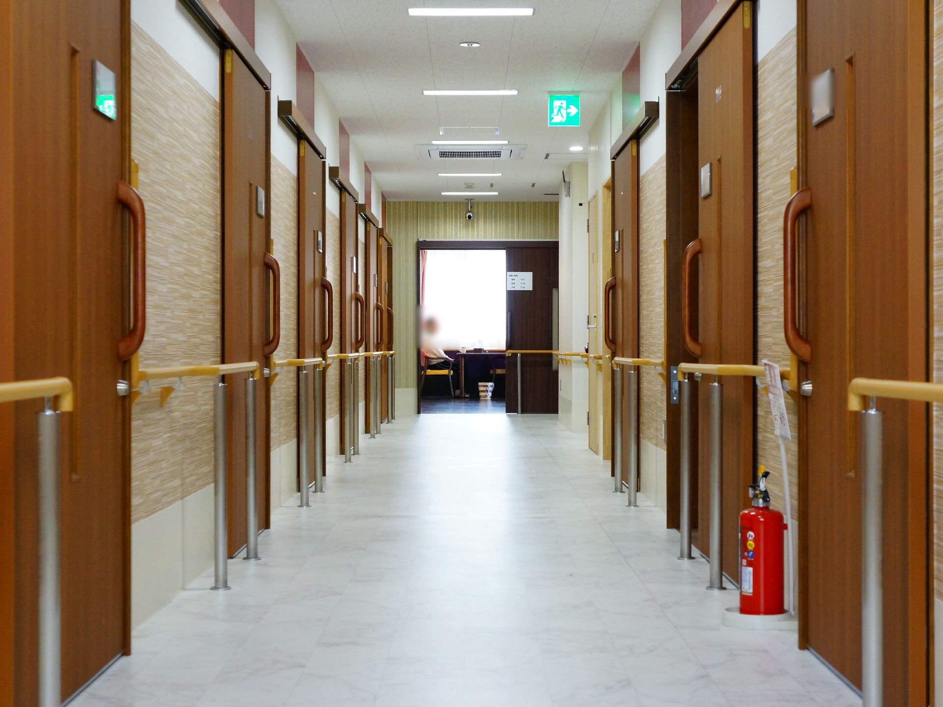 段差がなくフラットな廊下の床にはポールが設置され、その上部に手すりが設置されている。両側には部屋のドアが並んでいる。