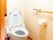 白色の洋式便座が備え付けられた、清潔感あるトイレである。壁の手すりを利用しながら、安全に使用することができる。