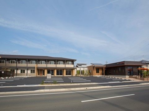 ダークブラウンが基調の２階建ての建物である。周辺は広々とした空間が広がっており、駐車スペースがたくさん用意されている。