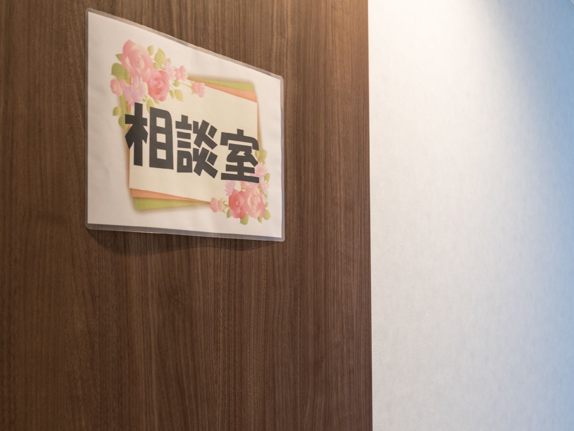相談室のドアのアップ画像。ドアは濃い茶色の木目調。花の付いたフレームデザインの中に「相談室」の文字が描かれた紙が貼ってある。