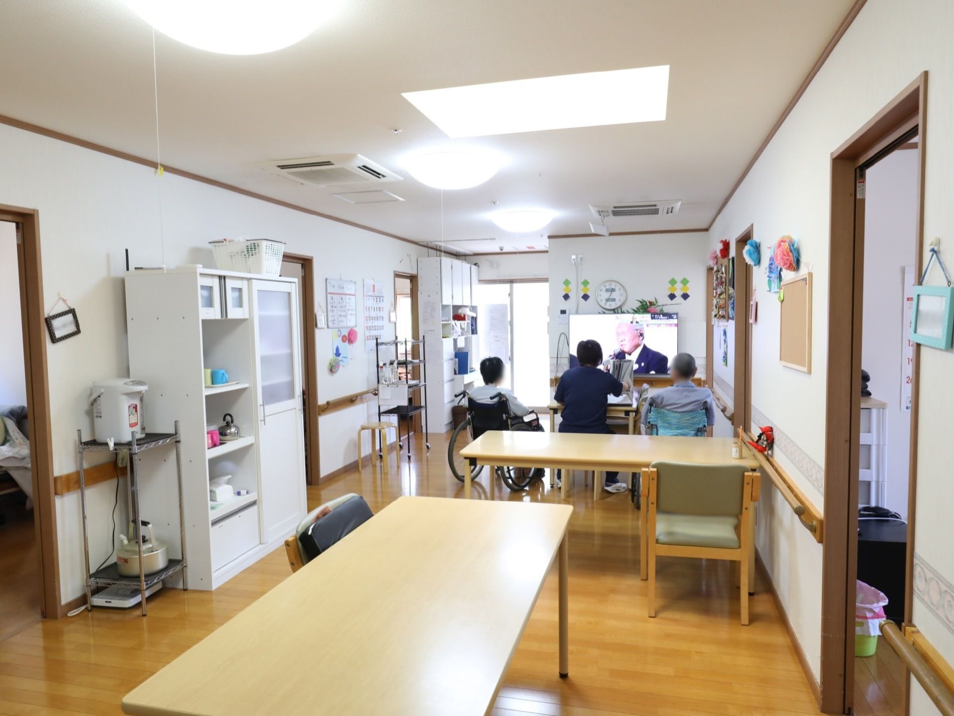 縦に長いフロアの壁際に白い食器棚が設置されている。奥にはテレビが置かれており、食事以外でも入居者様がくつろげるスペースになっている。